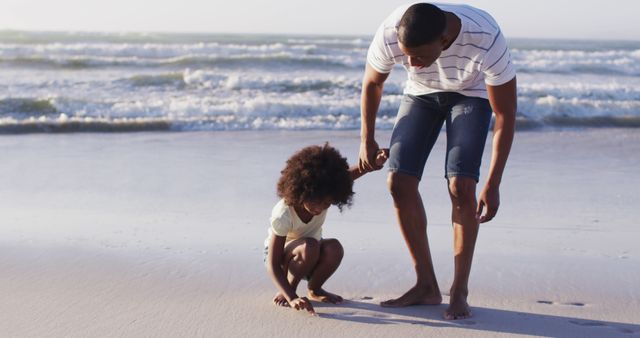 Parent and child spending quality time on sandy beach next to ocean waves. Ideal for use in family vacation, parenting, and lifestyle content.