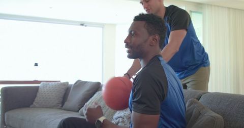 Diverse friends watching basketball game on sofa holding ball in modern living room