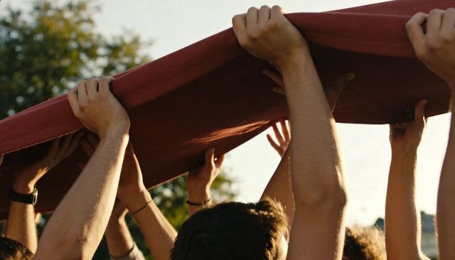 Friends lifting red blanket overhead during golden hour outdoor teamwork