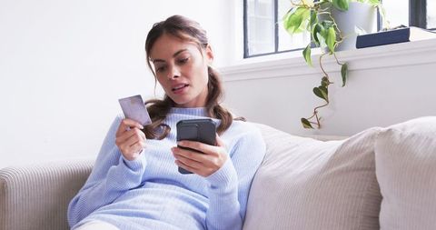 Woman checking her smartphone and credit card at home