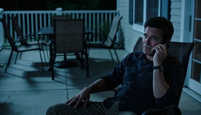 Middle-aged man on patio holding smartphone during reflective late-night call