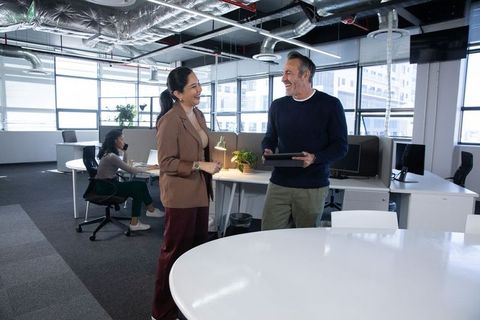 Coworkers smiling and chatting in modern open office while holding tablet