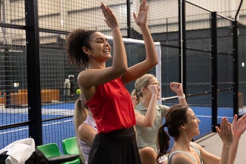 Diverse women cheering on padel court | team celebration and supportive spectating