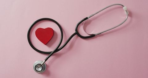 Stethoscope encircling red heart on soft pink background