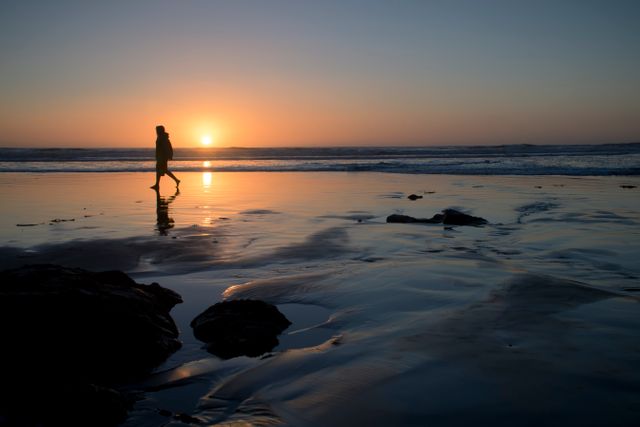 Person walking alone on beach during sunset creating a peaceful and reflective ambiance. Suitable for themes involving solitude, meditation, relaxation, and natural beauty.