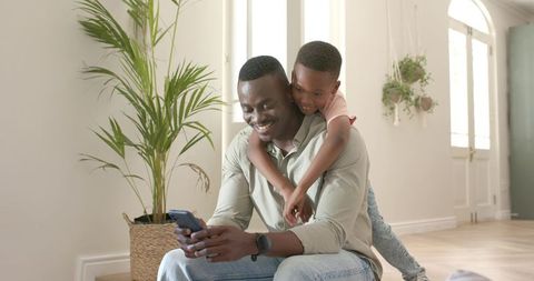 African american father and son sharing smartphone moments in bright minimal home interior