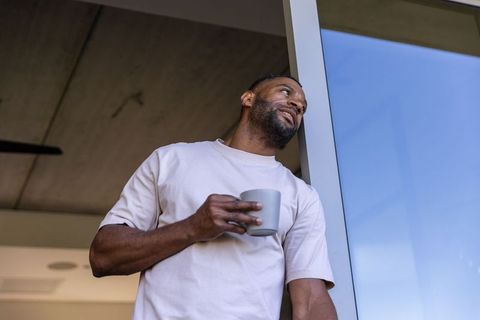 Mature african american man leaning in doorway holding mug, gazing upward, minimalist home