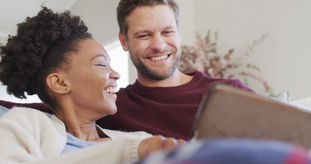 Image of happy diverse couple embracing and using tablet on sofa. Love, relationship and spending quality time together at home.