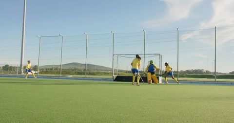 Female field hockey team practices penalty corner drill on turf