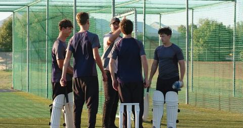Coach guiding youth cricket team during net practice with batting pads and stumps