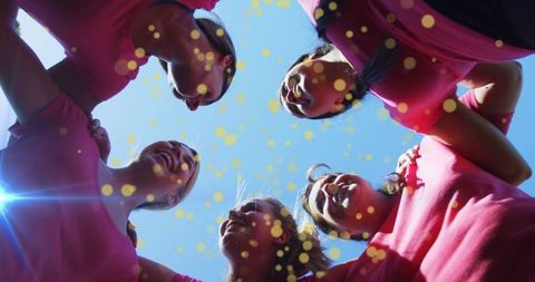 Women linking arms and celebrating unity in pink shirts under clear blue sky
