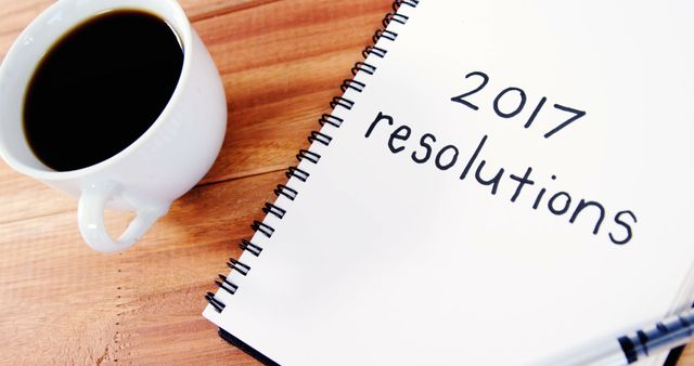 2017 resolutions text on notebook with cup of black coffee on wooden background and copy space. New year's resolutions, improvement and wish list concept.
