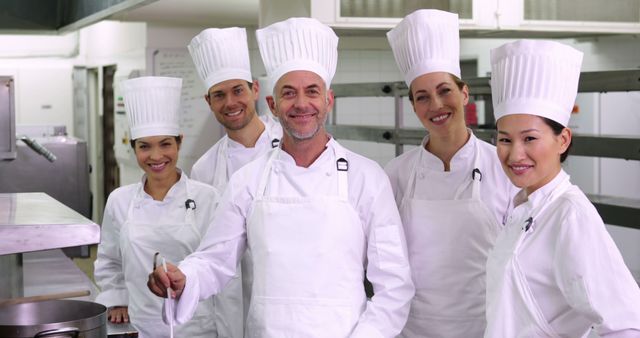 Group of professional chefs dressed in white uniforms and chef's hats standing together in a kitchen, smiling confidently. Perfect for showcasing culinary team spirit, restaurant marketing, and emphasizing professional expertise in culinary arts. Ideal for use in chef recruitment advertisements, culinary school brochures, and food industry websites.