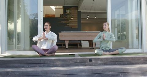 Two women practicing yoga on deck in prayer pose with smartphone between mats