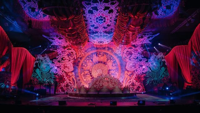 Illuminating ornate mandala stage featuring dramatic red drapes and floral centerpiece