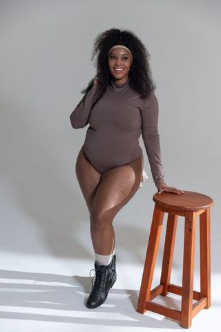 Curvy african american woman standing and posing wearing long-sleeve bodysuit and boots