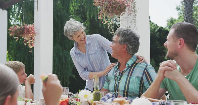 Happy caucasian family sitting at table in garden, eating dinner and talking. Lifestyle, domestic life, family, and togetherness.
