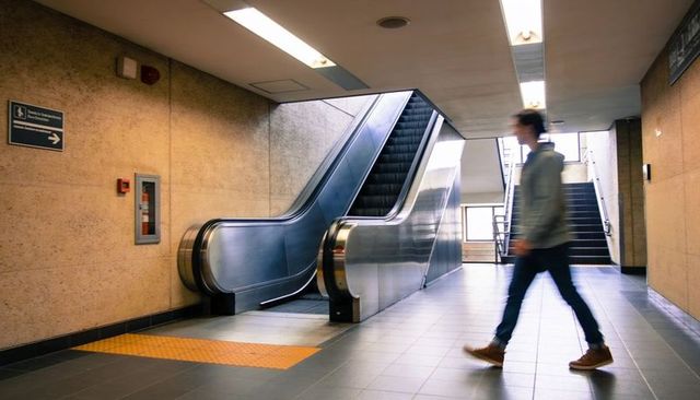 Modern subway concourse with stainless steel escalator and blurred commuter walking briskly