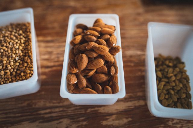 Open plastic containers of nuts, seeds and grains on worn wooden worktop at gin distillery. ingredients at an independent craft gin distillery business.