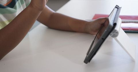 African american child using tablet on stand at white desk for remote learning
