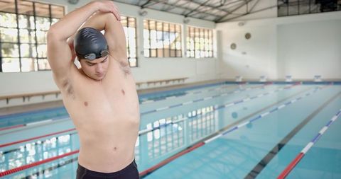 Male swimmer stretching next to indoor pool preparing for training