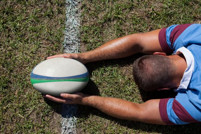 Rear view of rugby player holding ball on goal line at playing field