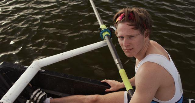 Young male athlete wearing white rowing gear rowing in single scull on calm lake. Ideal for illustrating themes of water sports, individual athletic training, perseverance, and outdoor activities or for use in sports-related promotions and advertisements.