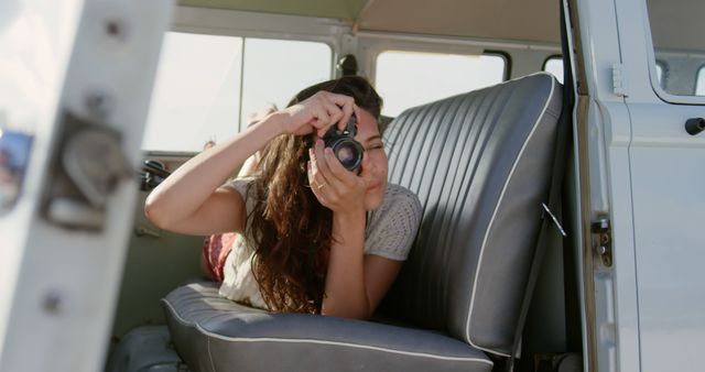 Young Caucasian woman captures memories from a vintage van. Her passion for photography shines through in this sunlit outdoor setting.