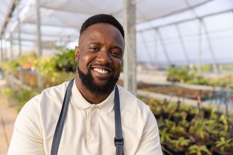 Smiling african american grower tending seedlings in bright commercial greenhouse