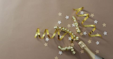 Celebrating with gold streamers and star confetti around champagne bottle neck flatlay