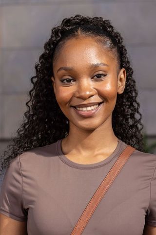 Confident black woman smiling in mauve top with leather crossbody strap, urban portrait