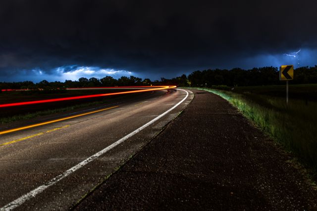 This captivating night scene with illuminated car light trails and a flash of lightning in the dark sky can be used for themes related to weather phenomena, road safety, travel, and adventure. Ideal for backgrounds, websites or blogs about stormy weather, travel photography, and road trips.