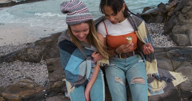 Two young women enjoying ice cream on rocky beach - Download Free Stock Images Pikwizard.com