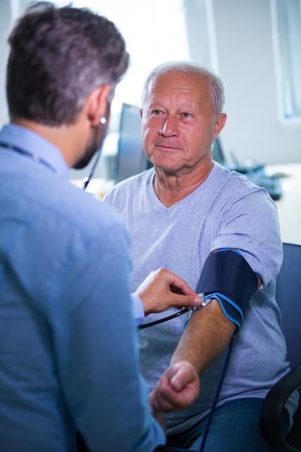 This image shows a male doctor checking the blood pressure of a senior patient in a hospital setting. It can be used for healthcare, medical, and wellness-related content, illustrating patient care, medical checkups, and doctor-patient interactions.