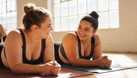 Plus-size women practicing yoga together on sunlit studio mats, smiling and breathing