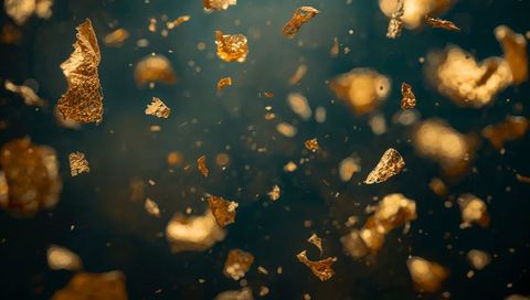 Floating Gold Leaf Flakes Catching Light Over Teal Background with Bokeh