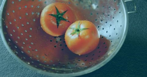 Juicy ripe tomatoes in stainless steel colander top view with water droplets for food prep