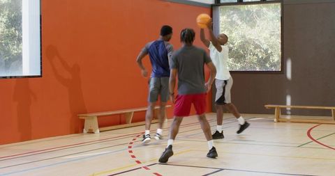 Three players practicing basketball offense in indoor gym with coach signaling drill