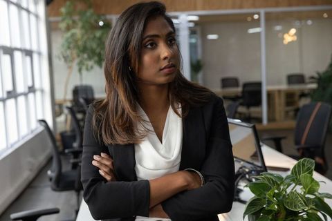Confident indian businesswoman standing arms crossed in modern open-plan office, leadership