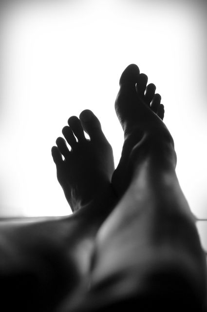 Silhouetted close-up of relaxed bare feet resting against a light background creating a tranquil atmosphere. This minimalist and intimate image is ideal for promoting wellness, relaxation, self-care, and lifestyle themes. Perfect for blogs, social media posts, spa websites, and health magazines.