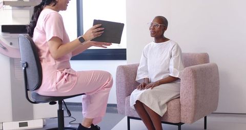 Nurse consulting with senior African American woman using tablet in clinic chair