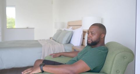 Man sitting on green armchair in minimalist bedroom checking smartwatch, morning calm