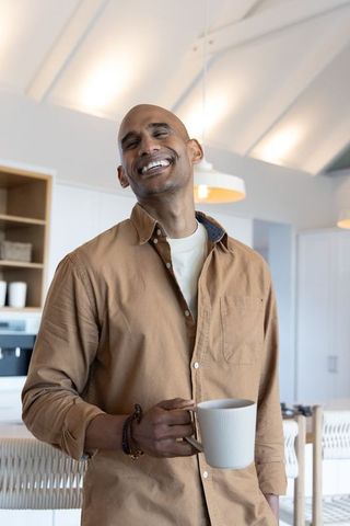 Smiling man enjoying morning coffee in bright modern rustic kitchen lifestyle portrait
