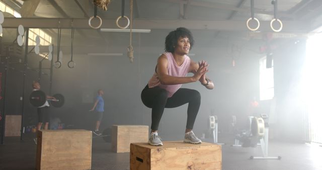 Woman performing box jumps in a gym, showcasing strength and fitness. Great for use in fitness magazines, training guides, and gym promotional materials. Highlights themes of health, exercise routines, and athleticism.