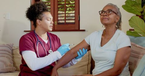 Nurse administering vaccine to senior woman at home
