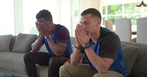 Diverse male friends showing disappointment seated on sofa wearing blue shirts and watches