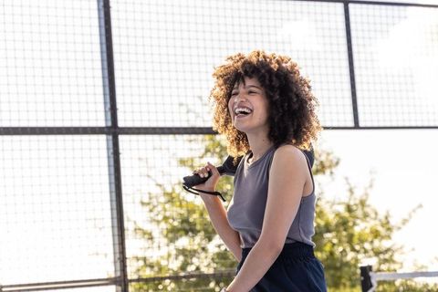Sunlit african american woman laughing while holding skateboard at outdoor court