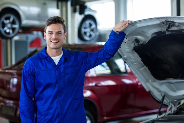 Portrait of smiling mechanic standing near car in repair shop