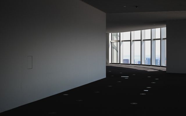 View of empty commercial office space with large windows letting in natural light. Ideal for illustrating modern architecture, real estate listings for office spaces, or depicting serene, minimalist working environments.