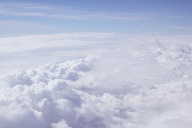 Soft white clouds viewed from above against a blue sky horizon. Perfect for themes associated with travel, serenity, nature, and sky-themed designs in both print and digital formats.